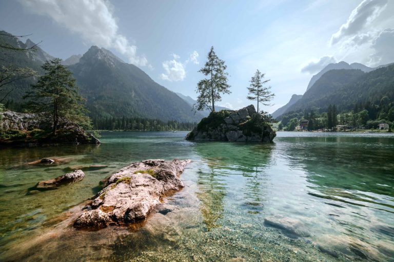 Kristallklarer See zwischen Bergen mit Bäumen und Felsen, Symbol für nachhaltige Wassernutzung.