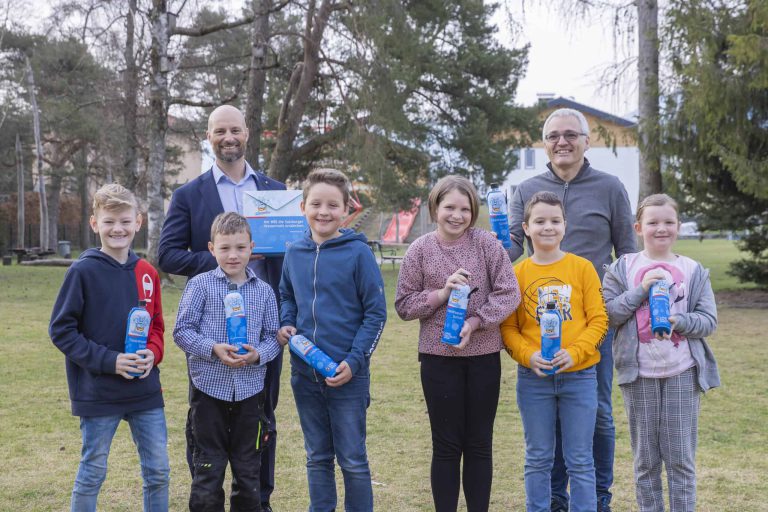 Schüler und Lehrer halten Trinkflaschen, feiern das Projekt TrinkWasser!Schule in Oberalm.